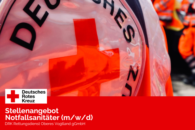Rückenansicht einer Jacke eines Notfallsanitäters mit DRK Abzeichen, im Hintergrund, verschwommen, weitere Notallsanitäter in Arbeitskleidung blau-orange.
