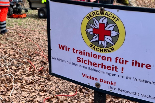 Schild mit dem Bergwachtlogo und der Aufschrift: Wir trainieren für Ihre Sicherheit.