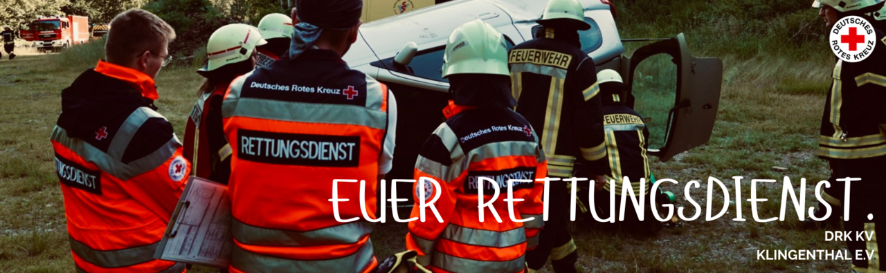 Mitarbeiter der DRK Rettungsdienst Oberes Vogtland gGmbH stehen mit dem Rücken zum Fotografen und beobachten die Feuerwehr im Rahmen einer Übung bei der Sicherung eines verunglückten Pkw.
