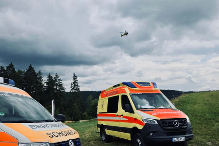 Der Manschaftswagen der Bergwacht Schöneck, ein Rettungswagen der DRK Oberes Vogtland gGmbH stehen auf einer Wiese in der Bike Welt. Der Rettungshubschrauber Christoph 46 ist schon in der Luft.
