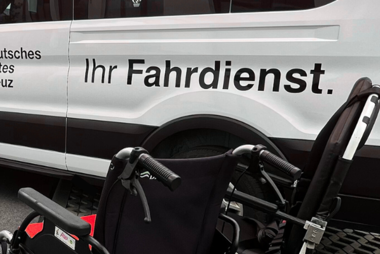 Ein Rollstuhl steht vor einem DRK Fahrdienst Transporter mit der Aufschrift Ihr Fahrdienst