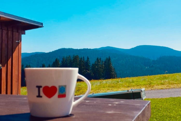 Eine Espresso Tasse steht auf dem Tisch der Bergwacht Horska Sluzba in Bublava. Dahinter sind die Berge des Erzgebirges zu sehen.